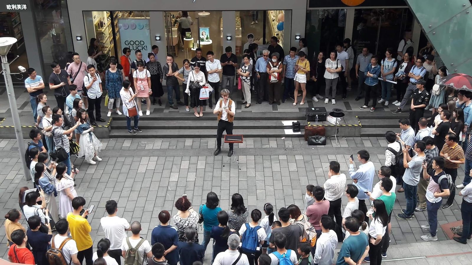 Overhead view of a large crowd forming a circle around Sam King performing a street show in Shanghai, China
